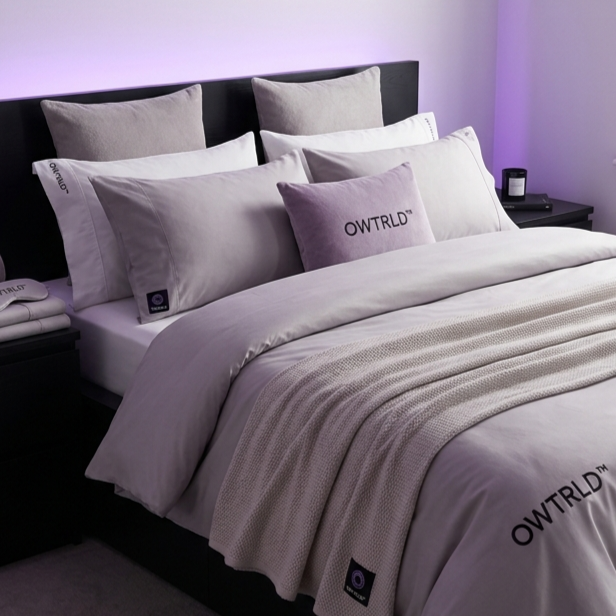 A beautifully styled, modern bedroom featuring crisp white and neutral-toned OWTRLD bedding, with soft morning light hitting a plush duvet and pillows
